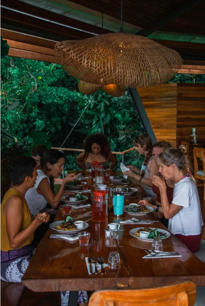 Friends enjoying communal dining experience at The Jungle Lodge open-air restaurant with sustainable local cuisine surrounded by tropical rainforest atmosphere and ambiance