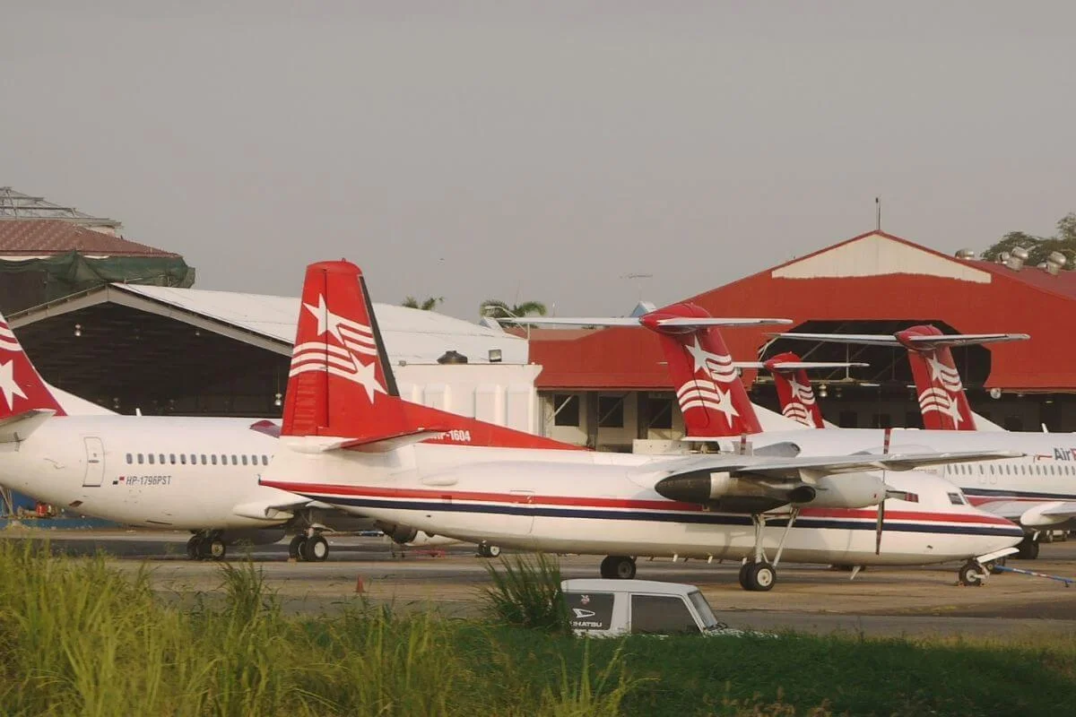 Several Air Panama regional aircraft with distinctive red and white star livery parked on the tarmac at Albrook Airport in Panama City, with red-roofed airport hangars and palm trees in the background under an overcast sky.